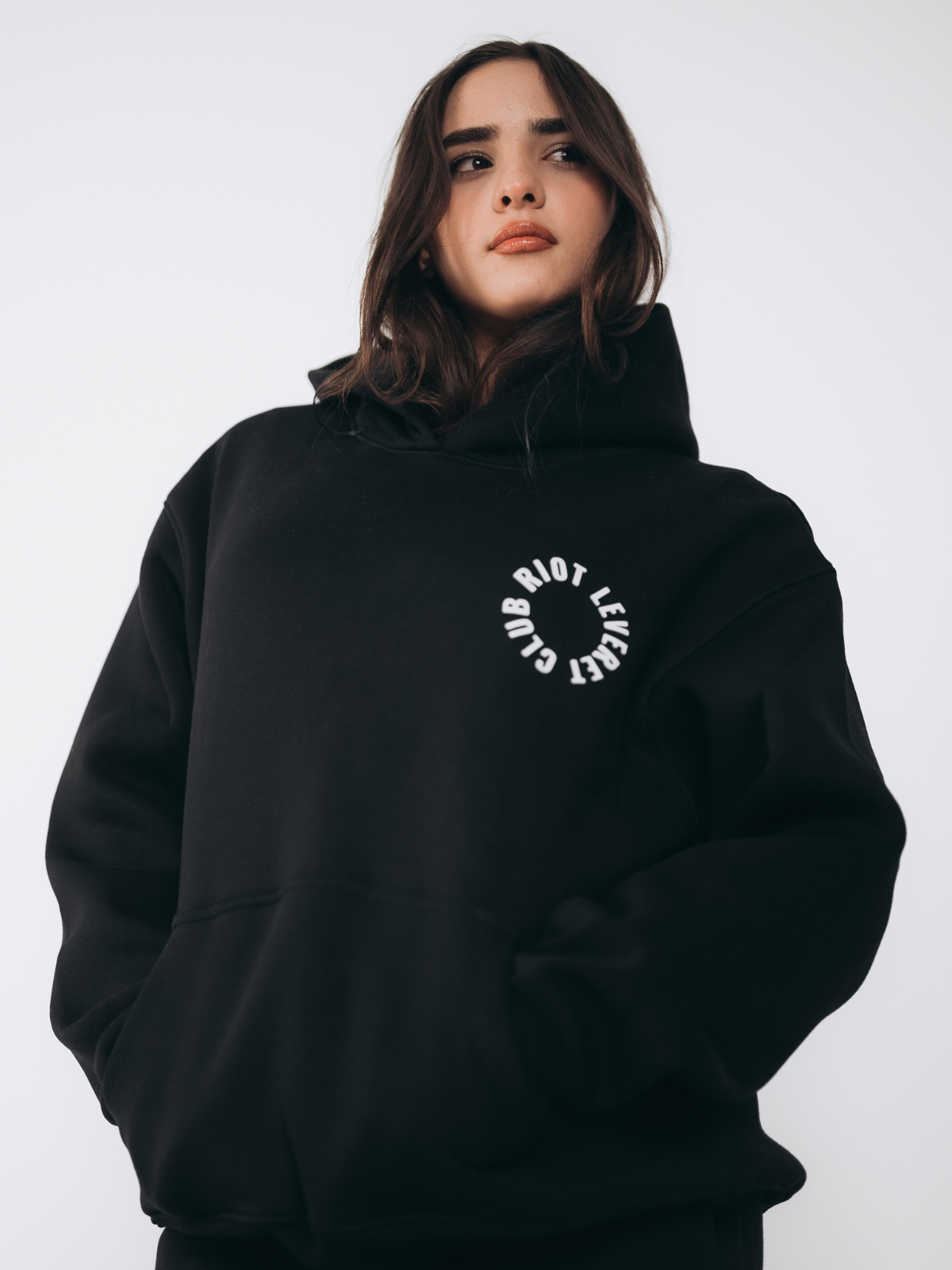 Model wearing the Riot Leveret Club black hoodie with bold white logo prints, showcasing a relaxed and trendy unisex fit for ultimate comfort and style.