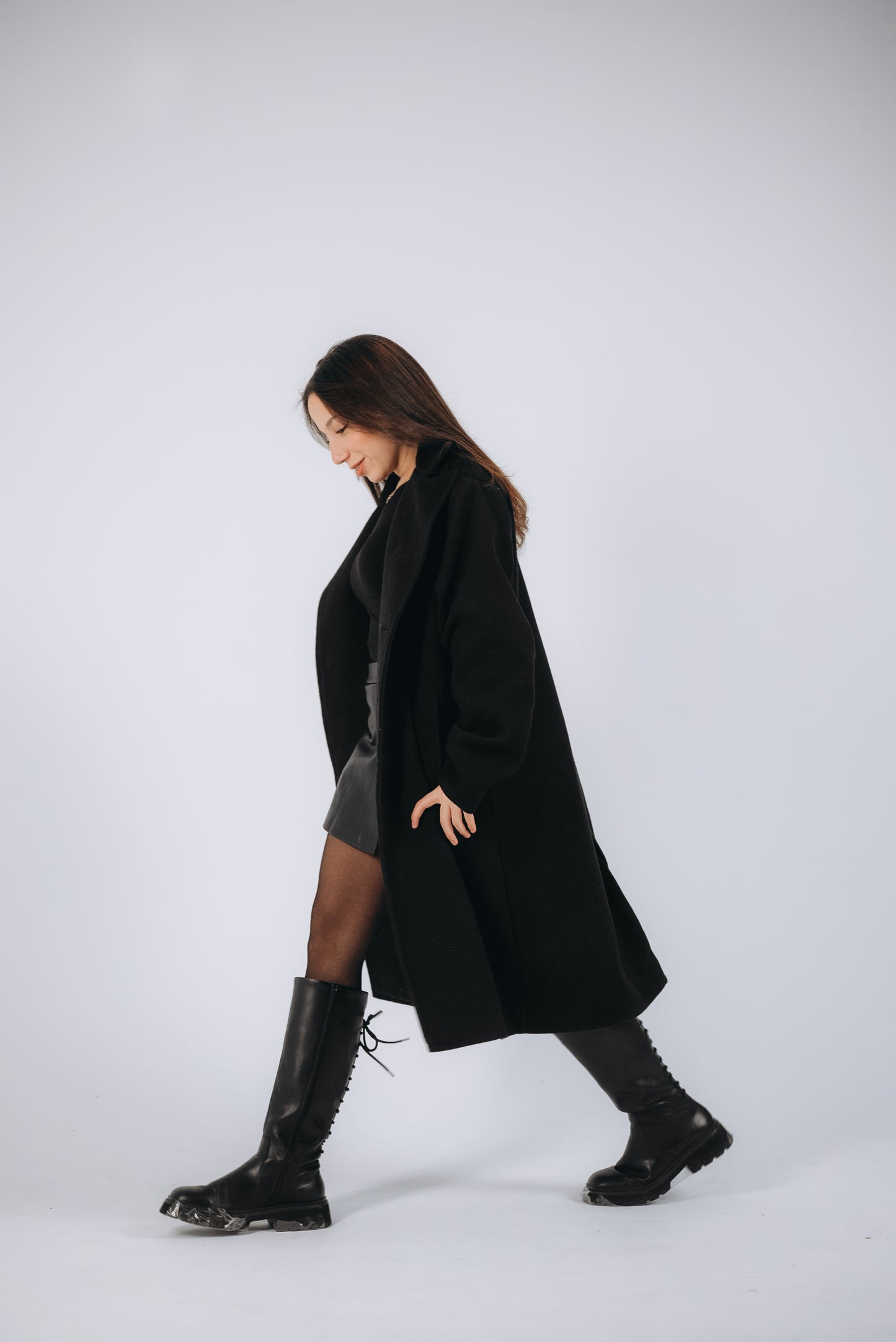 a model wears an oversized black coat- high neck boots in black