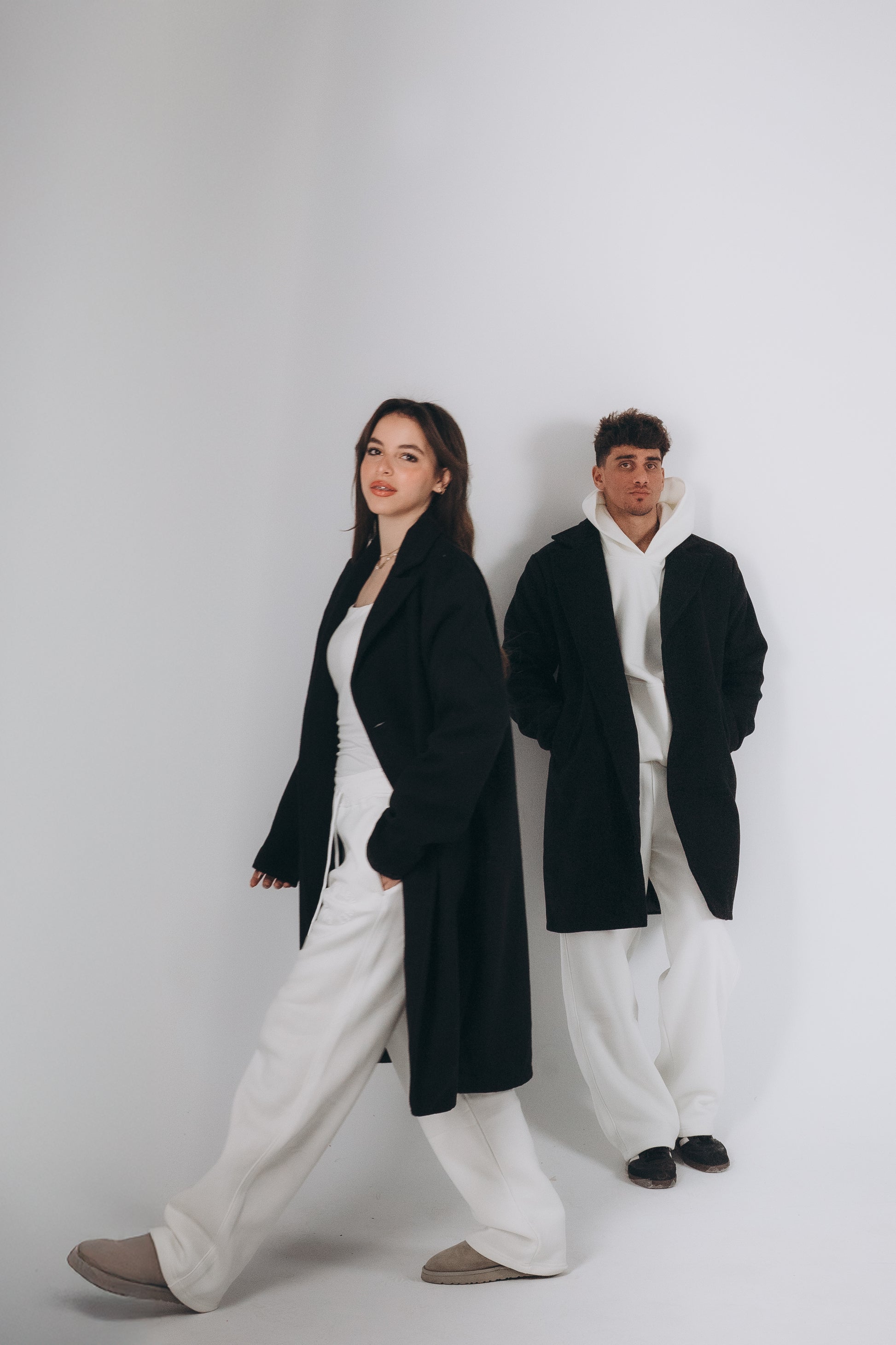 Two models are wearing oversized black coat layering with white set of hoodies and sweatpants 