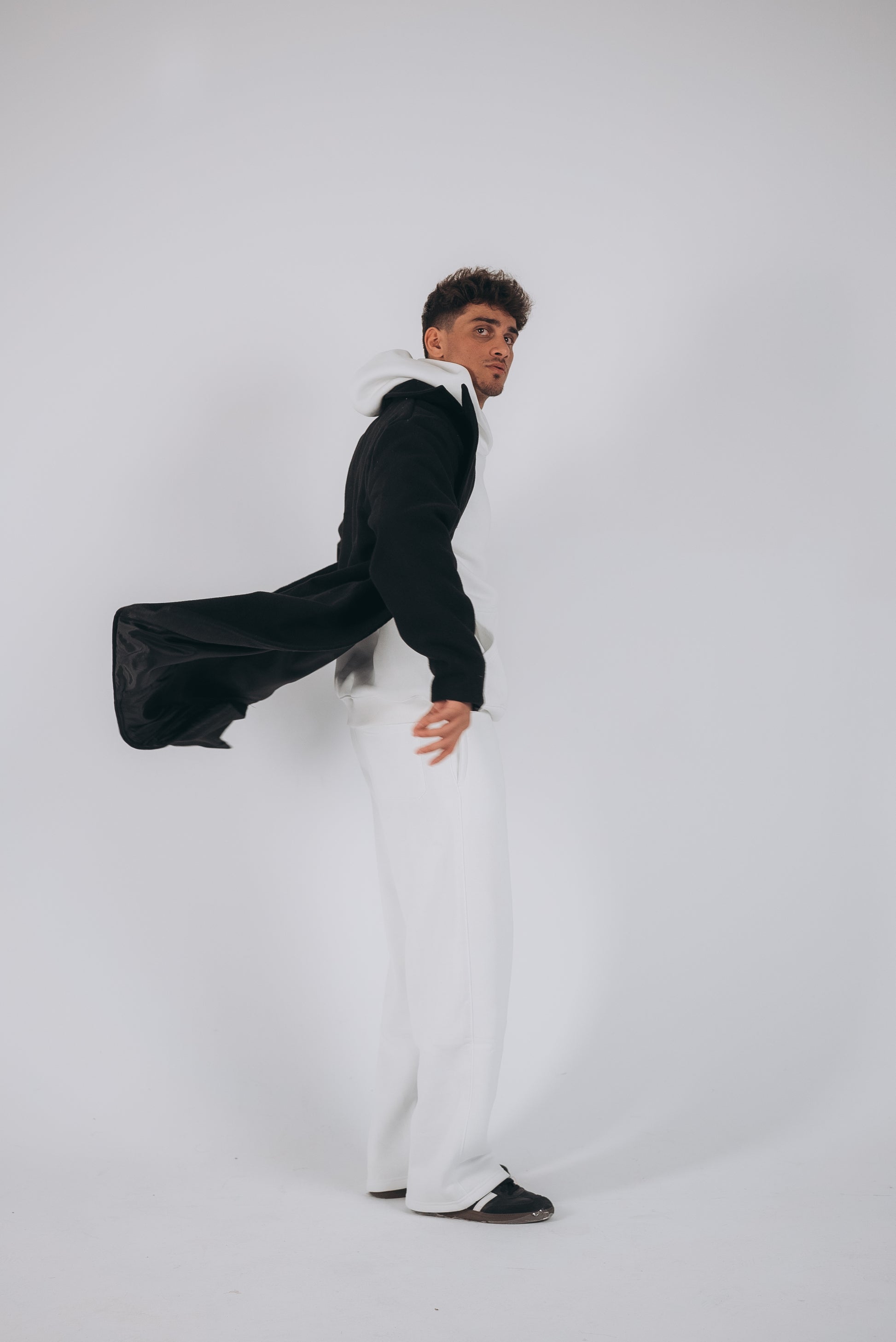 a model with white oversized set and white background showing the black coat with back movement 